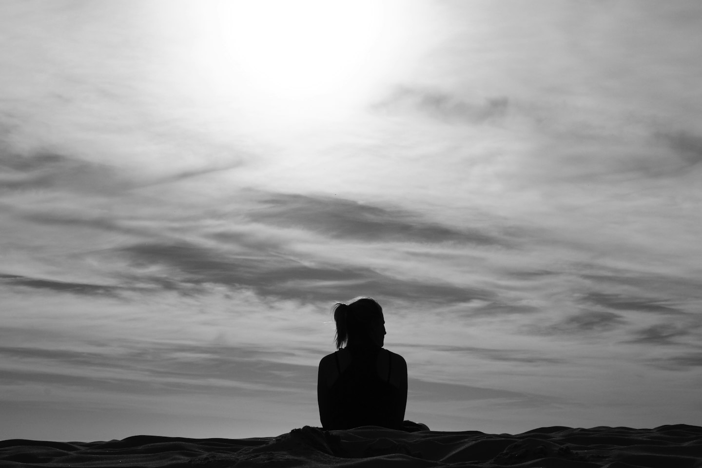 Silhouet van een persoon op een heuvel die naar een bewolkte lucht kijkt.
